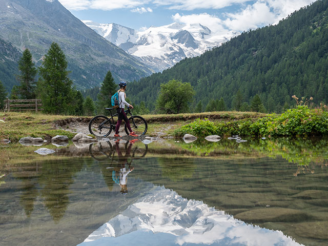 Frau auf dem Mountainbike an einem alpinen Seeufer blickt auf einen Gletscher